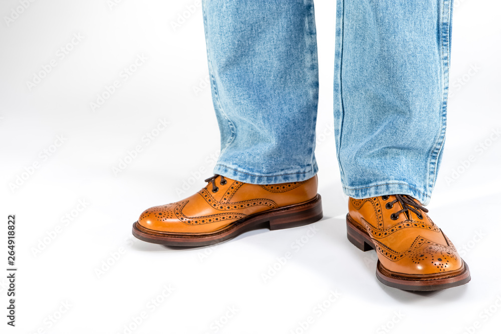 Closeup of Mens Legs on Brown Oxfords Brogues Shoes. Posing in Blue Jeans Against White Background