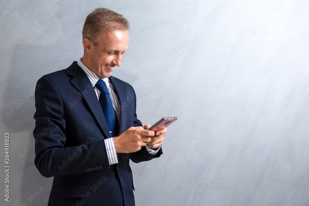 Portrait of Happy Caucasian Man in Blue Suit Holding Red Cellphone in Hands. Against Gray Grunge Wall. Portrait of Happy Caucasian Man in Blue Suit Holding Red Cellphone in Hands. Against Gray Grunge Wall.