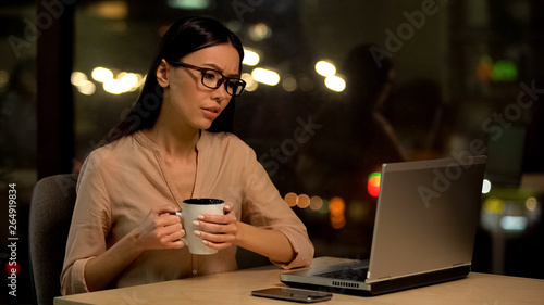 Sad female worker reading email holding cup of tea, job difficulties, mistake