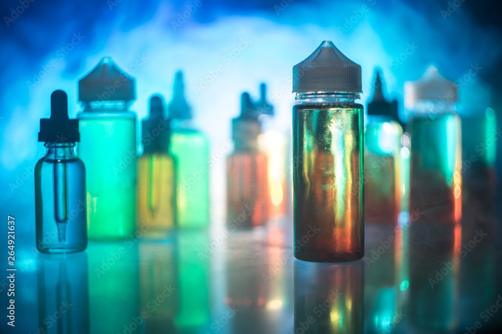 Vape concept. Smoke clouds and vape liquid bottles on dark background. Light effects. Useful as background or electronic cigarette advertisement. Vape concept. Smoke clouds and vape liquid bottles on dark background. Light effects. Useful as background or electronic cigarette advertisement.