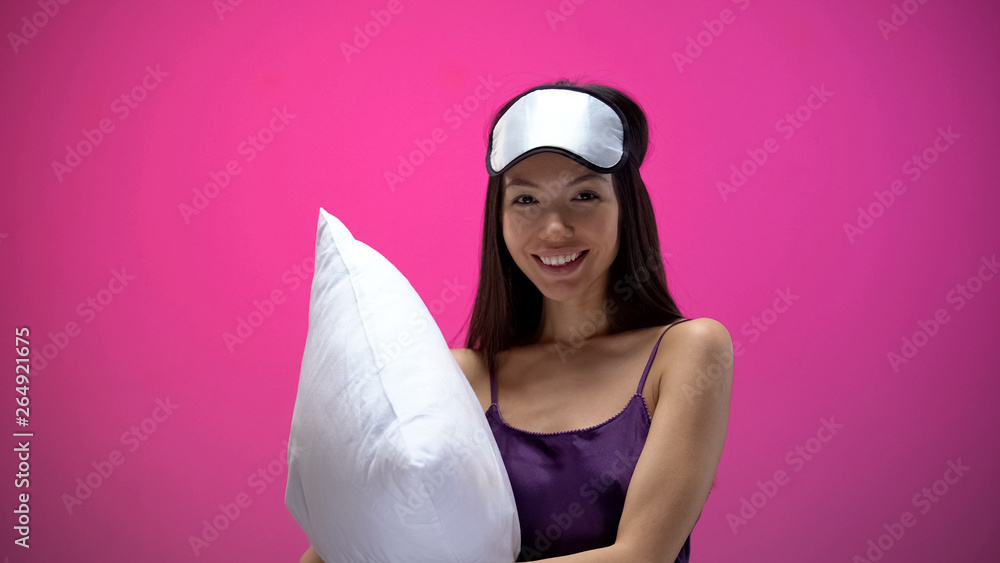 Smiling asian woman in eye mask holding pillow and smiling, preparing for sleep Smiling asian woman in eye mask holding pillow and smiling, preparing for sleep