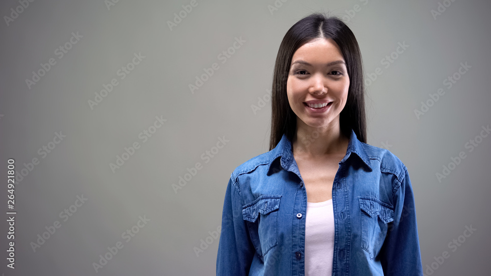 Beautiful asian female smiling, standing against grey background, place for text Beautiful asian female smiling, standing against grey background, place for text
