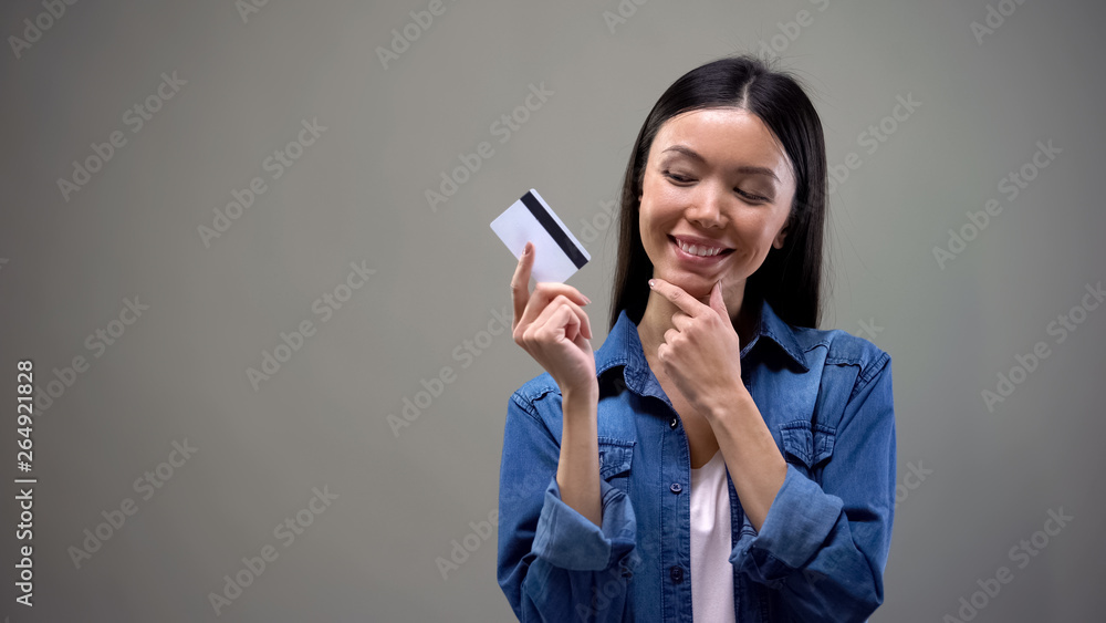 Smiling asian woman holding credit card and thinking about shopping, no limits Smiling asian woman holding credit card and thinking about shopping, no limits