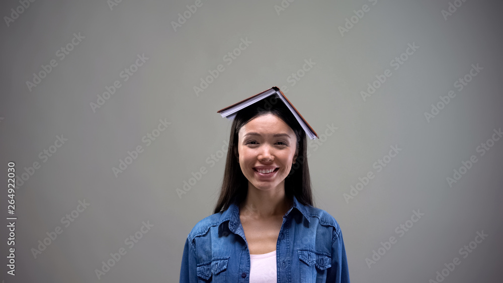 Laughing woman with book on head, having fun, grey background, place for text Laughing woman with book on head, having fun, grey background, place for text