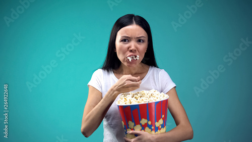 Obraz na plátne Focused on movie woman devouring popcorn from big paper cup, unhealthy eating
