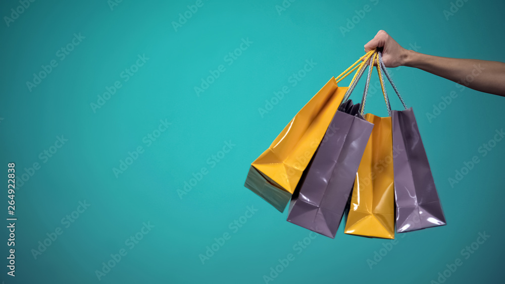 Female hand holding many colorful shopping bags on blue background, template