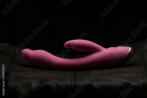 Pink dildo on black skin. Dark background. Artistic lighting.