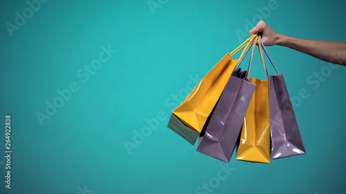 Female hand holding many colorful shopping bags on blue background, template photo