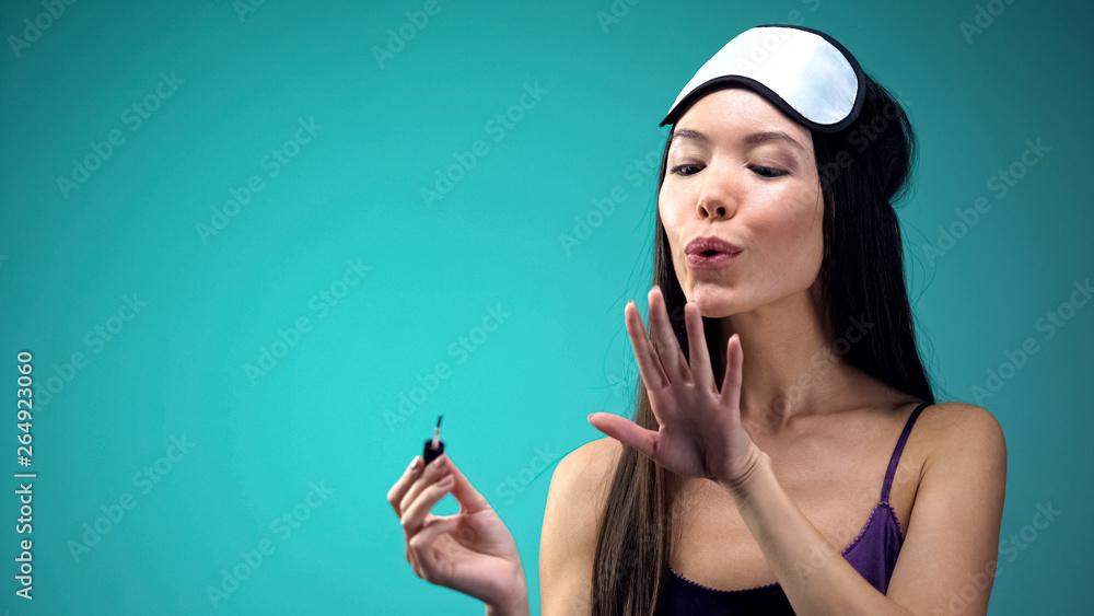 Pretty asian woman blowing on nail polish, wearing pajamas and blindfold, care Pretty asian woman blowing on nail polish, wearing pajamas and blindfold, care