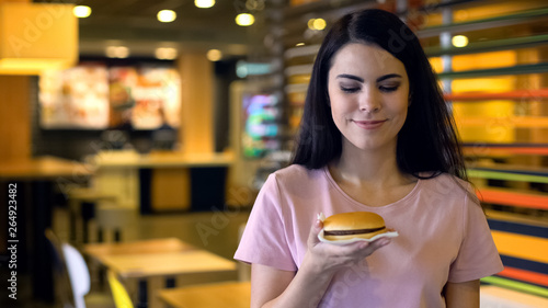 Happy female looking at tasty burger in hand, sandwich club, unhealthy nutrition
