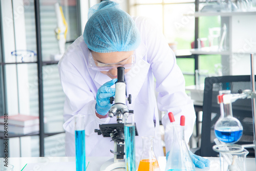 Asian woman scientist, researcher, technician, or student conducted research or experiment by using microscope which is scientific equipment in medical, chemistry or  biology laboratory