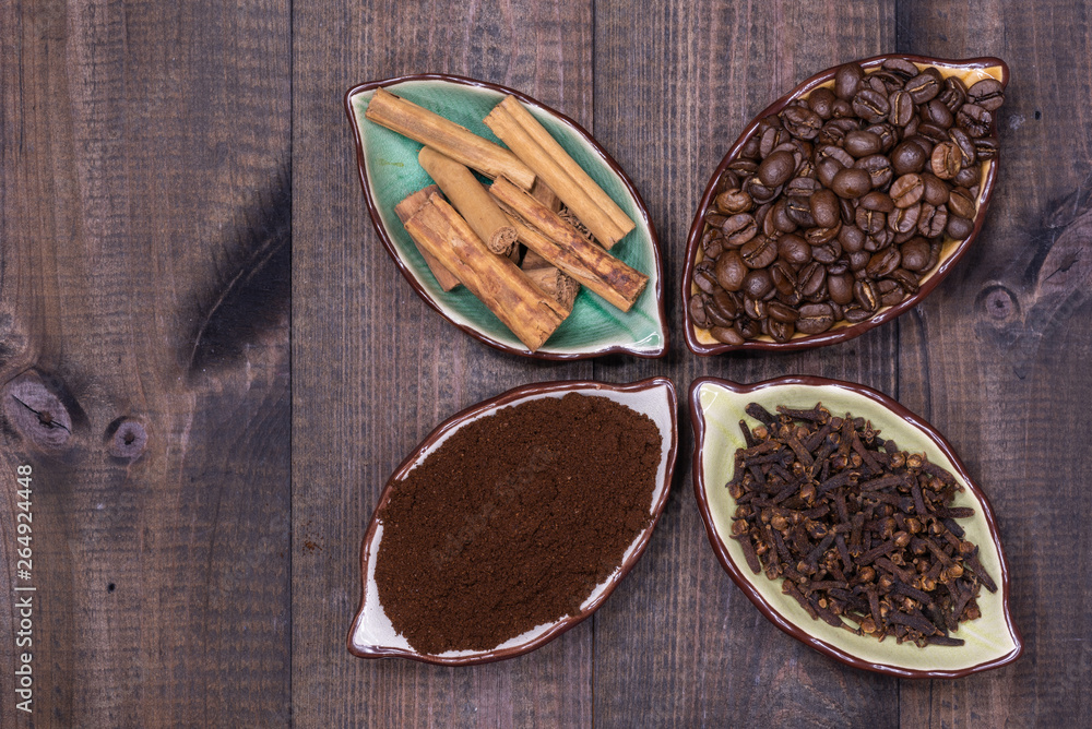 Four cups with coffee beans, cinnamon, cloves and coffee powder