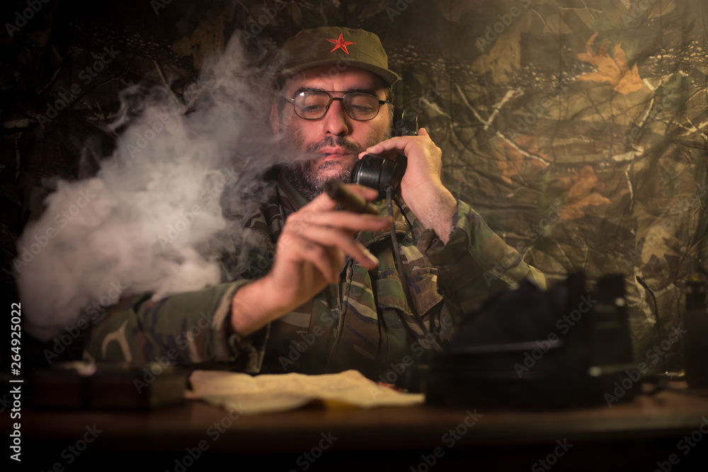 The evil dictator sitting on table. Angry communist general sitting at headquarter or Cuban commander in dark room.