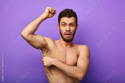 crying shirtless man waxing his armpits to depilate hair. close up photo.isolated blue background.