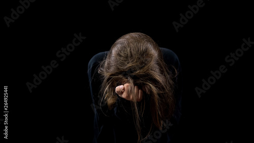 Desperate marital abuse victim crying looking down on black background, horror