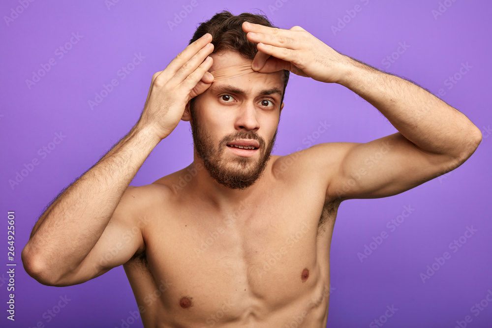 brutal shirtless bearded man using adhesive plaster. close up portrait.isolated blue background.handsome man sticking plaster on his face to hide a scar brutal shirtless bearded man using adhesive plaster. close up portrait.isolated blue background.handsome man sticking plaster on his face to hide a scar