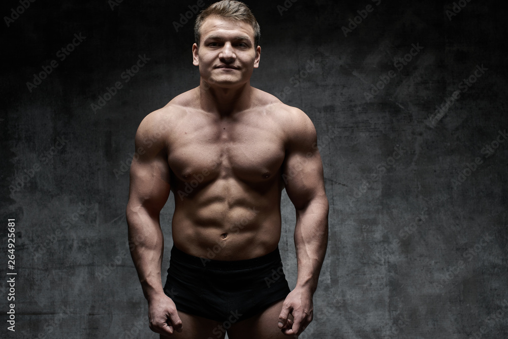 Sexy bodybuilder man posing on dark background in black shorts. Handsome pumped male body isolated with free space for advertising Sexy bodybuilder man posing on dark background in black shorts. Handsome pumped male body isolated with free space for advertising