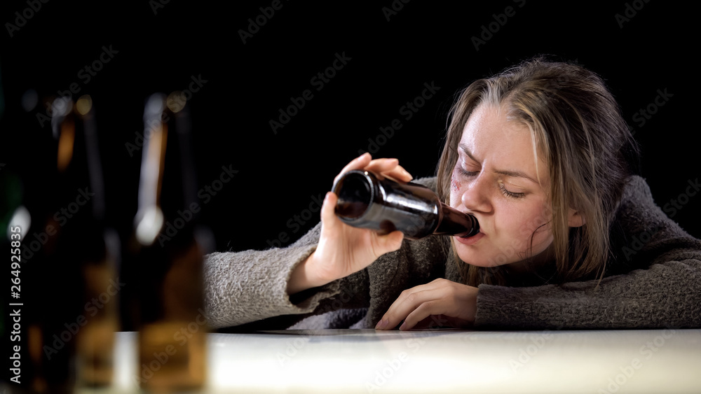 Addict woman lying on table and drinking beer, suffering hangover, hopelessness Addict woman lying on table and drinking beer, suffering hangover, hopelessness