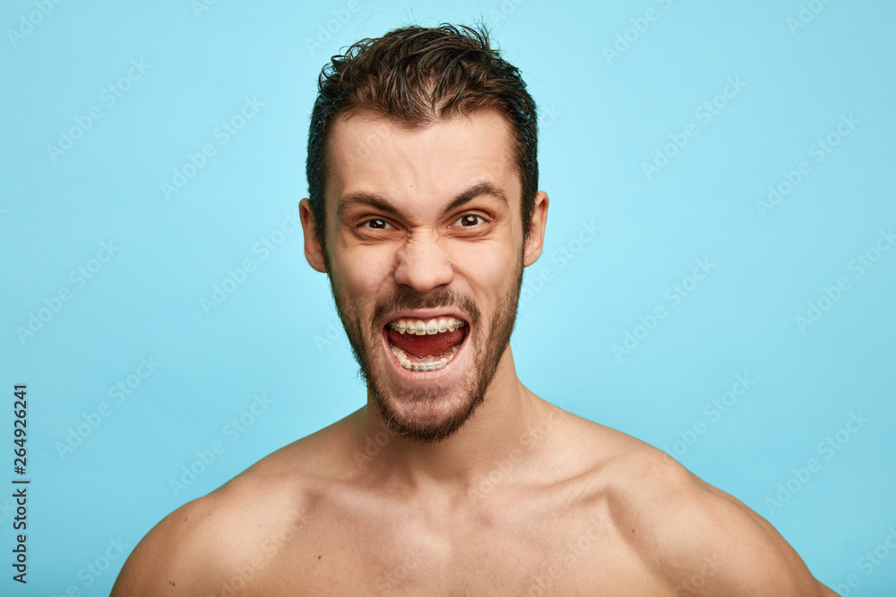 Furious shirtless man with grumpy grimace on his face,with mouth opened in shout, shows negative emotions, feeling, isolated over blue background Furious shirtless man with grumpy grimace on his face,with mouth opened in shout, shows negative emotions, feeling, isolated over blue background