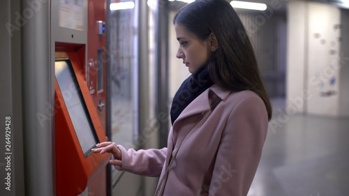 Fotografie Young female tourist buying tickets in self-service terminal, making payment