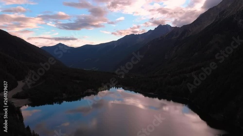 Aerial, rising, drone shot, of a mirroring lake, surrounded by alp mountains and forest, on a sunny evening sunset, at Lago Di Anterselva, in Parco Naturale Vedrette di Ries Aurina, south Tirol, Italy photo
