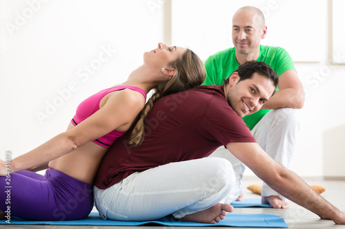 Personal trainer looking at couple doing yoga pose