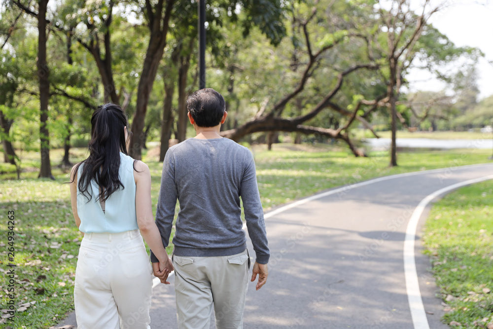 Obraz premium back view asian couple walking and talking in the park with happy face