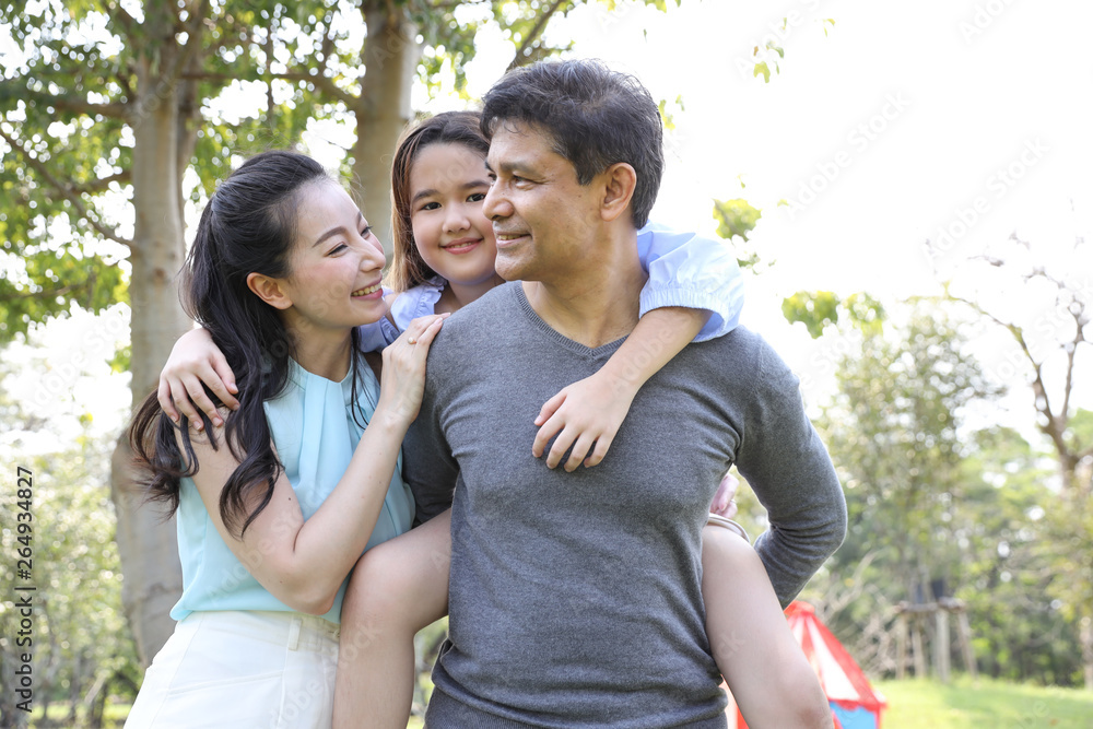 image of happy family, daughter riding behind father while parents smiling during summer time in the park image of happy family, daughter riding behind father while parents smiling during summer time in the park