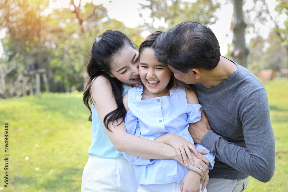 image of happy family, daughter putting her hands on parents cheek with smiling while father and mother kissing during summer time in the park image of happy family, daughter putting her hands on parents cheek with smiling while father and mother kissing during summer time in the park
