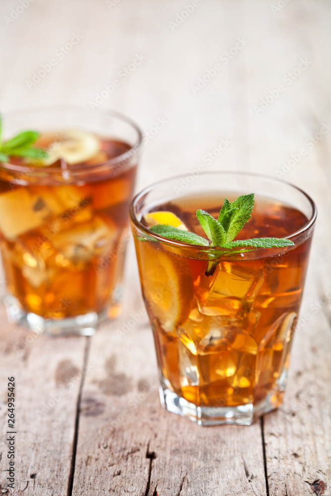 Two glasses with traditional iced tea with lemon, mint leaves and ice cubes in glass on rustic wooden table. Two glasses with traditional iced tea with lemon, mint leaves and ice cubes in glass on rustic wooden table.