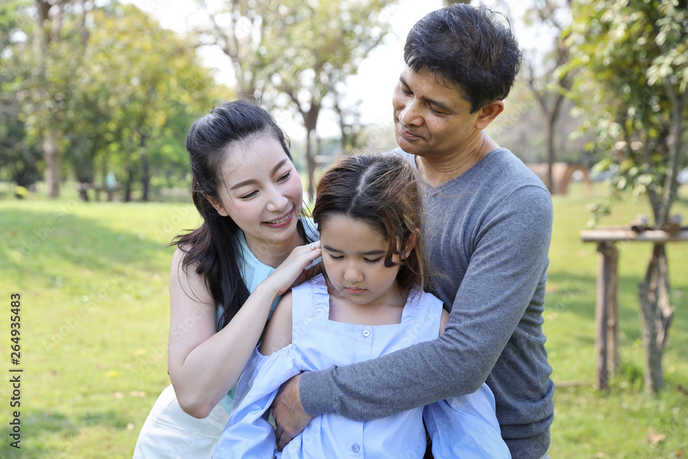 image of happy family, father and mother are comforting their depressed daughter with a smiling and warm face during holiday vacation in the park image of happy family, father and mother are comforting their depressed daughter with a smiling and warm face during holiday vacation in the park
