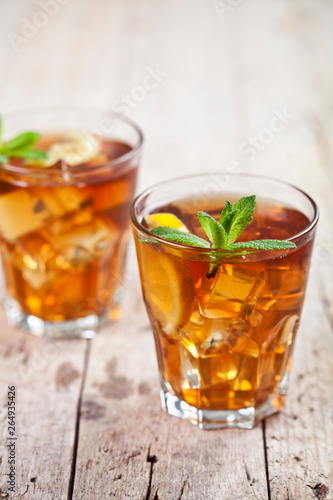 Two glasses with traditional iced tea with lemon, mint leaves and ice cubes in glass on rustic wooden table.