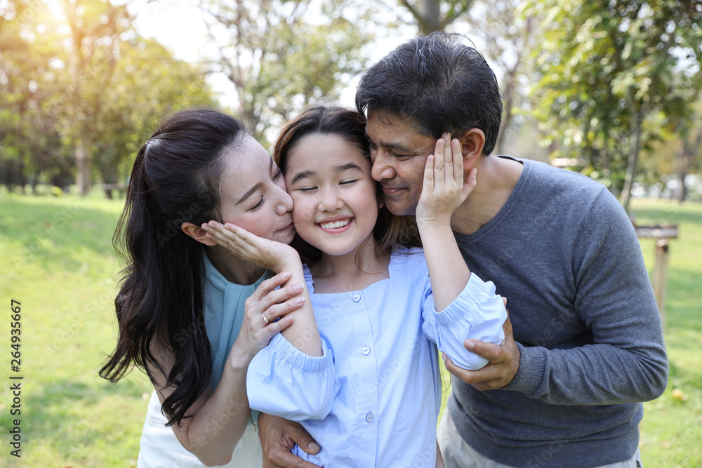image of happy family, daughter putting her hands on parents cheek with smiling while father and mother kissing during summer time in the park image of happy family, daughter putting her hands on parents cheek with smiling while father and mother kissing during summer time in the park