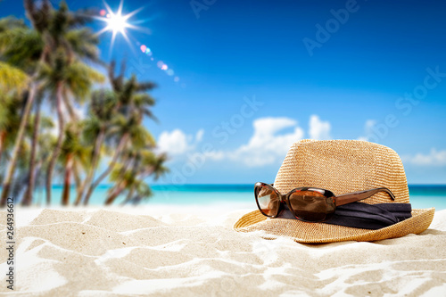 Summer sunglasses with hat on sand and blue towel. Free space for your decoration. Blurred background of beach with palms and ocean 