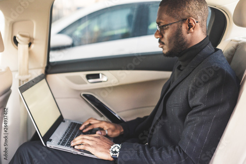 Man in a business suit write on laptop in the salon of an expensive car with leather interior. © xartproduction