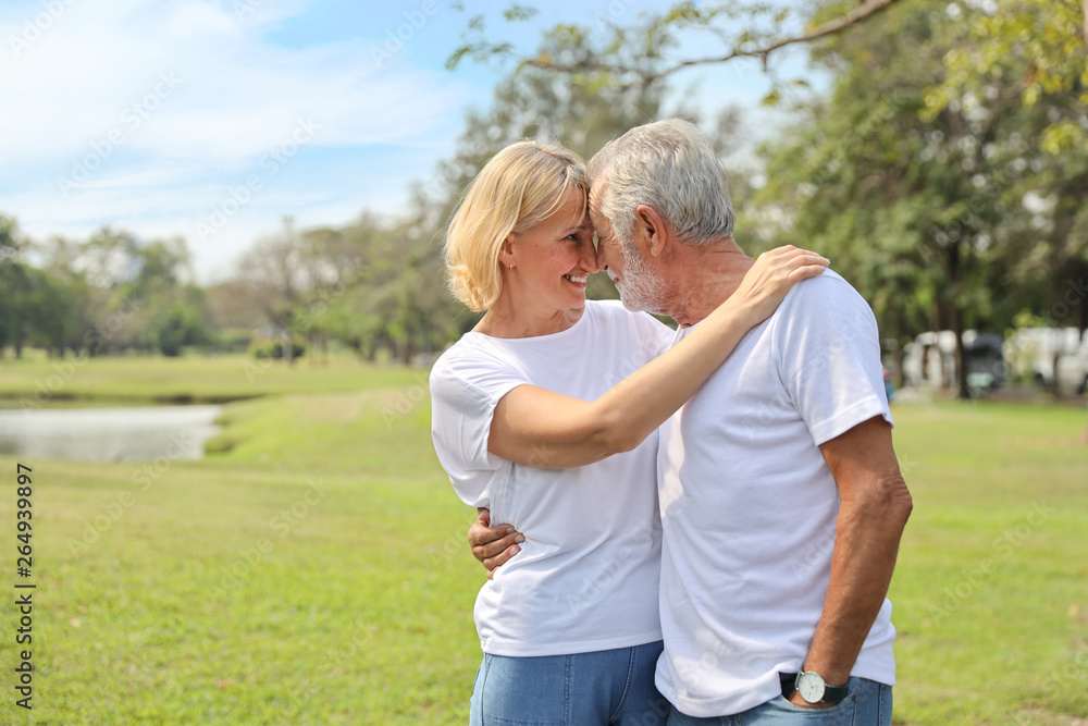 smiling elderly couple with white shirt and blue jean embracing in park in autumn time with sun light effect smiling elderly couple with white shirt and blue jean embracing in park in autumn time with sun light effect
