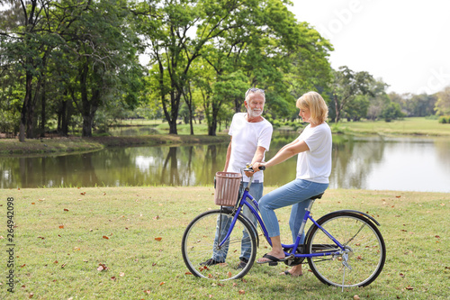 senior man and woman riding bicycle in the park on weekend with relaxation and smile face (elder healthy concept)