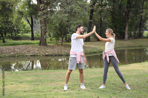 young and healthy couple people enjoying in exercising outdoor and they posting give me five with green trees during summer time in the park © feeling lucky