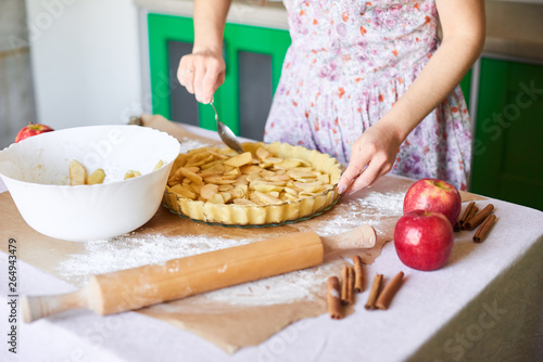 woman adds sliced apples to apple pie. Woman hands working a pie dough in a tray, on a kitchen table, surrounded by pumpkin pie ingredients. Traditional pies baking