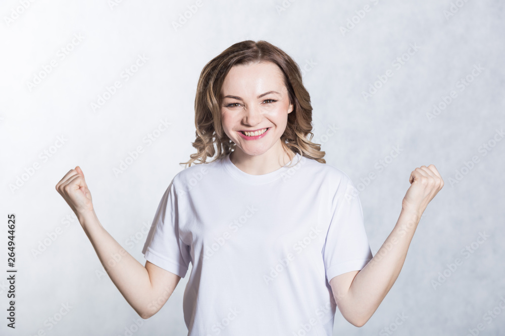 Portrait of overjoyed beautiful woman clenches fists with happiness, poses against white background. Portrait of overjoyed beautiful woman clenches fists with happiness, poses against white background.