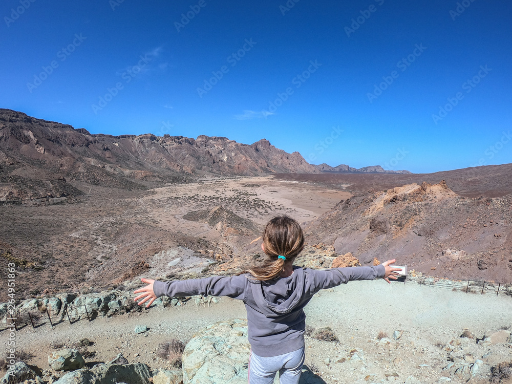 Cute little girl with arms wide open, wearing colorful coat, standing front corona forestal natural Park of Teide Tenerife. Atmosphere on top of mountain. Freedom and satisfaction goal achieved Cute little girl with arms wide open, wearing colorful coat, standing front corona forestal natural Park of Teide Tenerife. Atmosphere on top of mountain. Freedom and satisfaction goal achieved