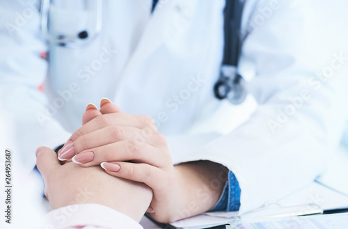 Friendly female doctor hands holding patient hand sitting at the desk for encouragement, empathy, cheering and support while medical examination. Just hands over the table.