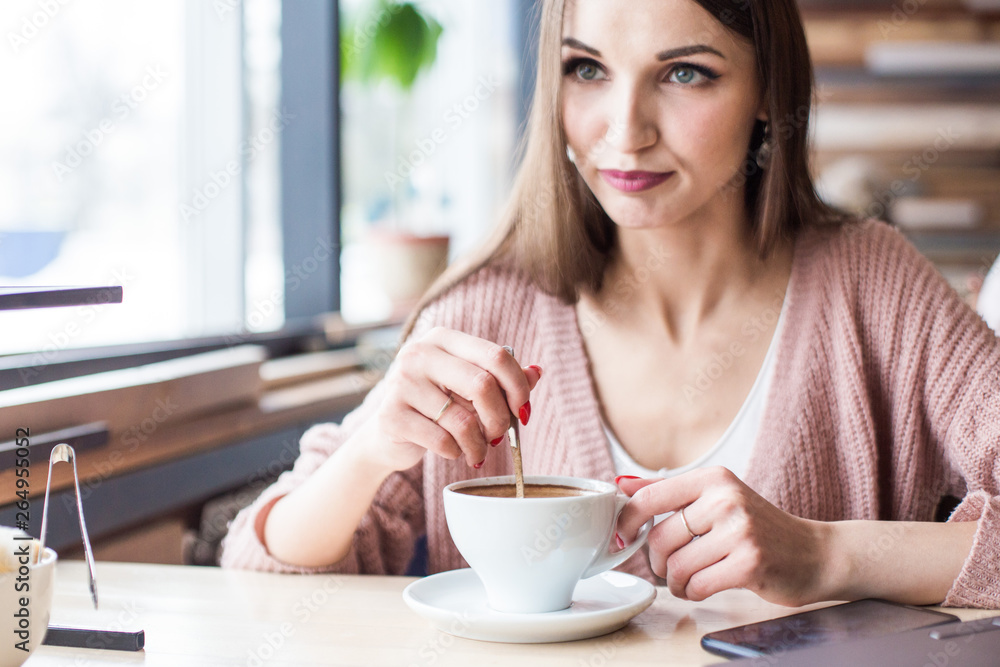 Beautiful young woman sits at a table in a cafe with a cup of coffee and looks out the window Beautiful young woman sits at a table in a cafe with a cup of coffee and looks out the window