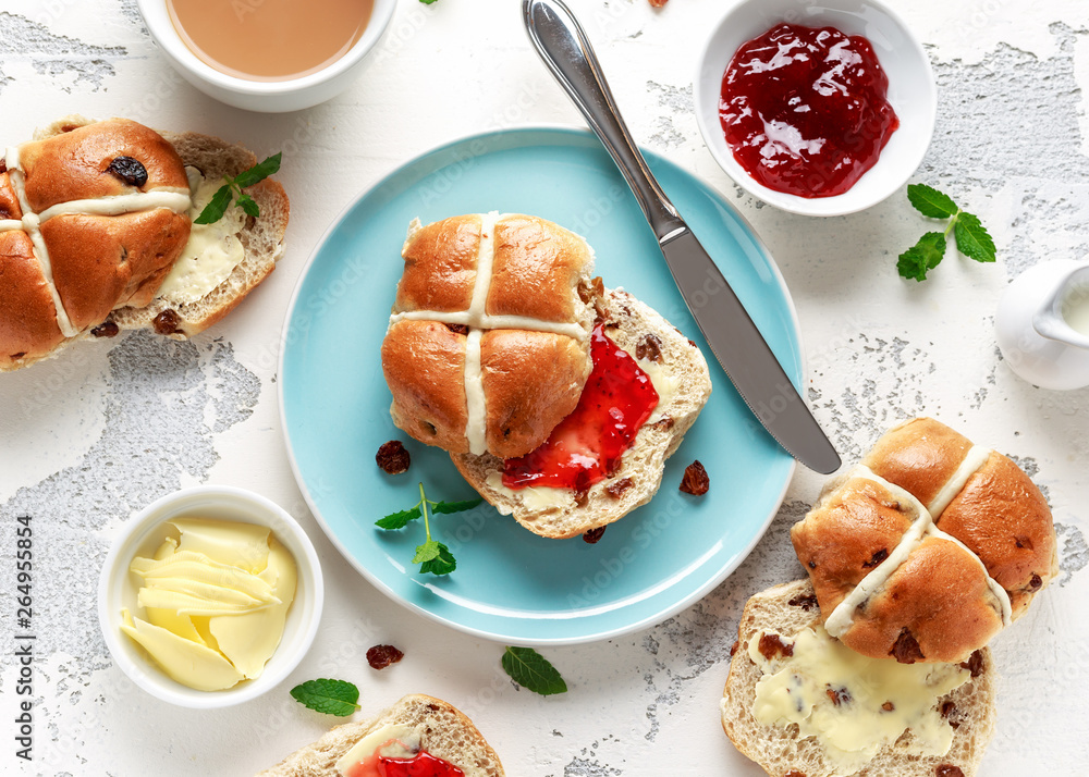 Hot cross buns in blue plate served with butter, strawberry jam and cup of tea Hot cross buns in blue plate served with butter, strawberry jam and cup of tea