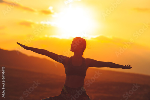 Silhouette of young woman practicing yoga or pilates at sunset or sunrise in beautiful mountain location. © davit85