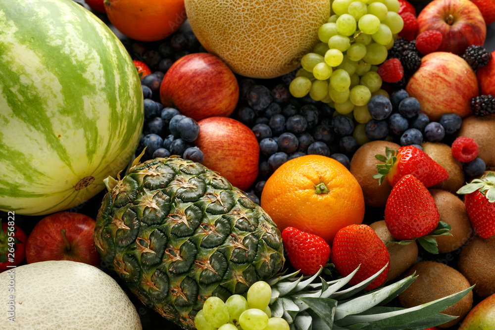 Variety of fresh fruits and berries on dark background: cantaloupe, melon, watermelon, blueberry, oranges, apple, strawberry, pineapple, mango, grapes and kiwi.