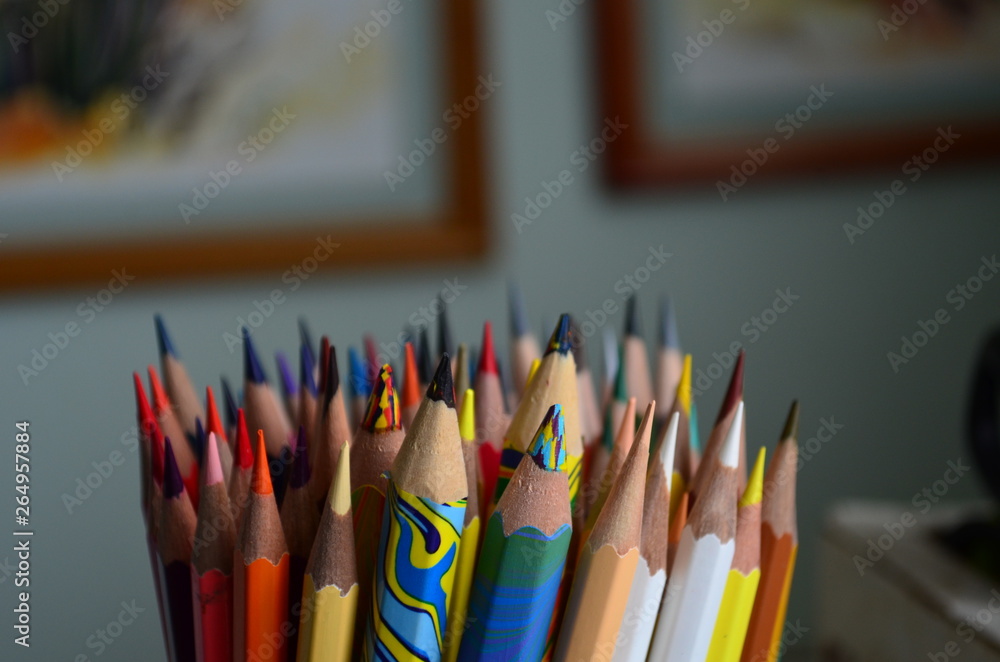 Fototapeta premium many colored pencils in the stand on the background of paintings