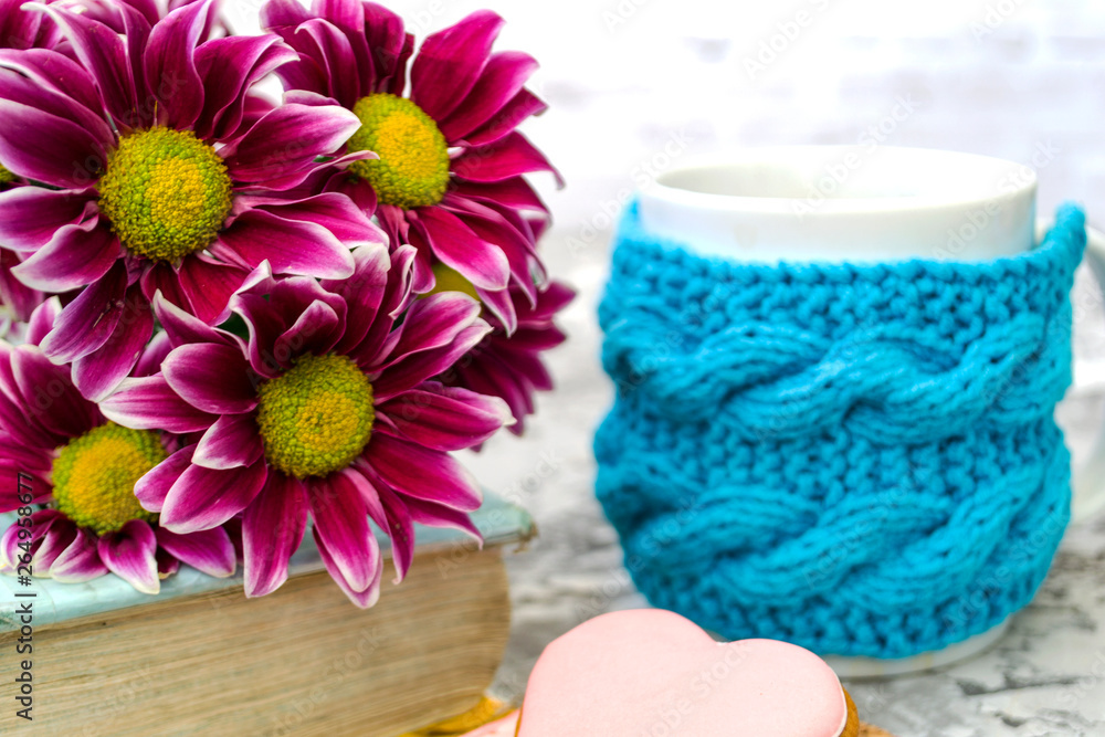 Maroon chrysanthemum. Pink flowers with a yellow center lie on the book. Nearby is a cup of tea, and delicious coffee. Pink gingerbread cookies are like dessert. Maroon chrysanthemum. Pink flowers with a yellow center lie on the book. Nearby is a cup of tea, and delicious coffee. Pink gingerbread cookies are like dessert.