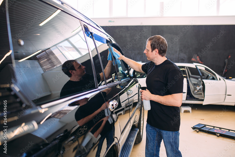 The man is wiping with a cloth body of a brilliant car. The man is wiping with a cloth body of a brilliant car.