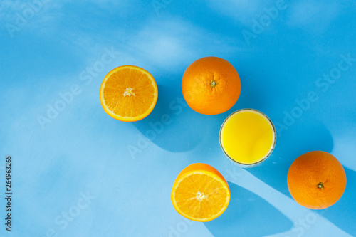 A glass of orange juice and oranges on a blue background. Concept of vitamins  tropic  summertime. Natural light. Flat lay  top view.